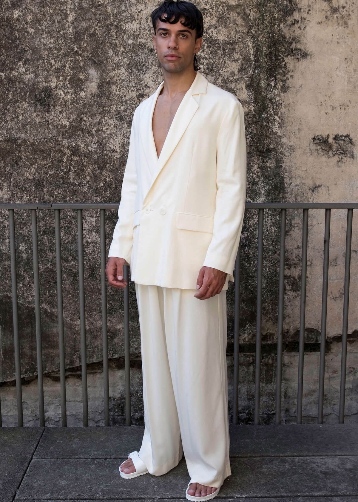 The Glade model wears a men’s double breasted blazer and mens high waisted pants in white